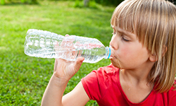 Ребенок пьет воду из бутылки в солнечный день